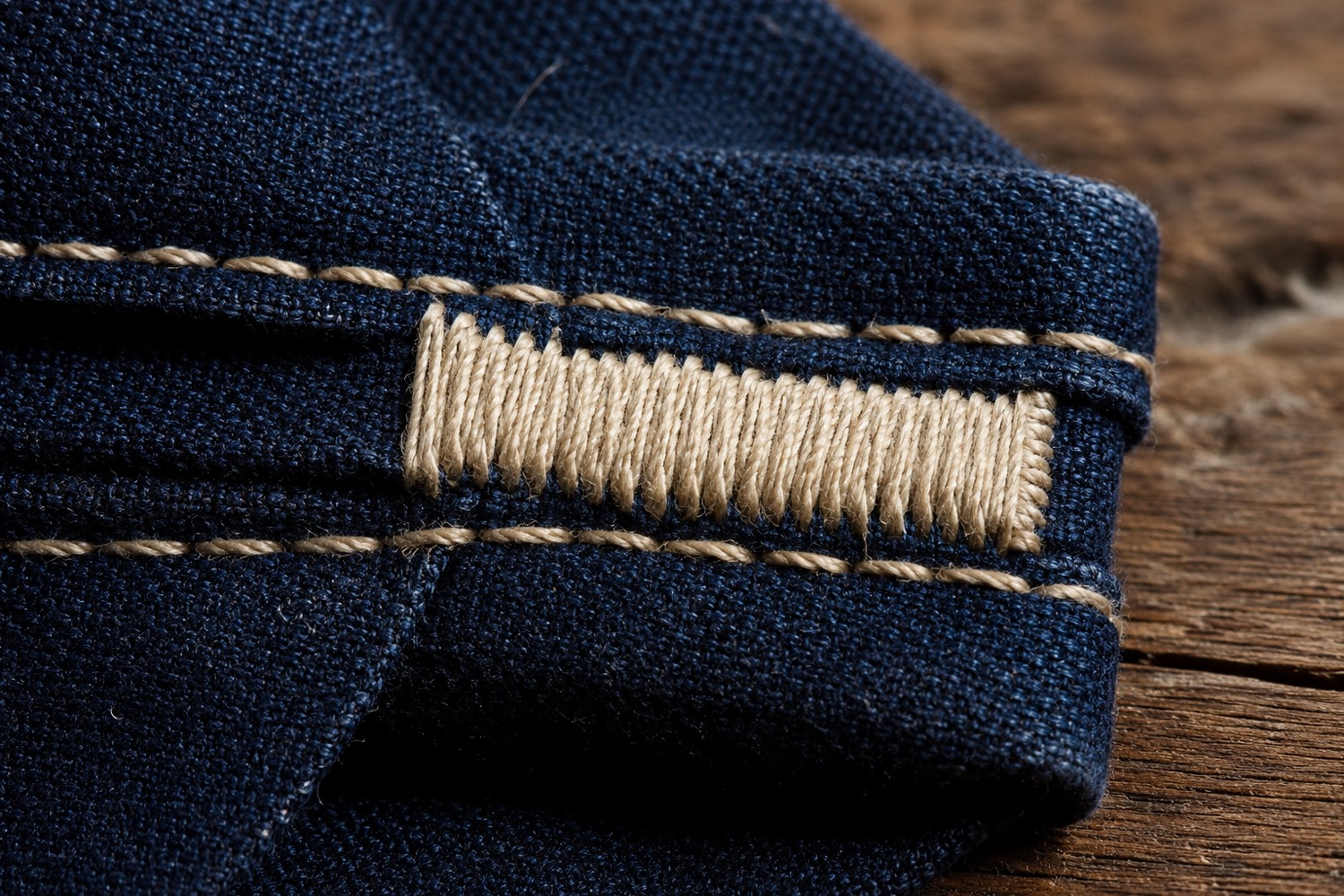 Extreme macro view of a bartack: a dense block of ecru stitching across a doubled seam of indigo canvas.