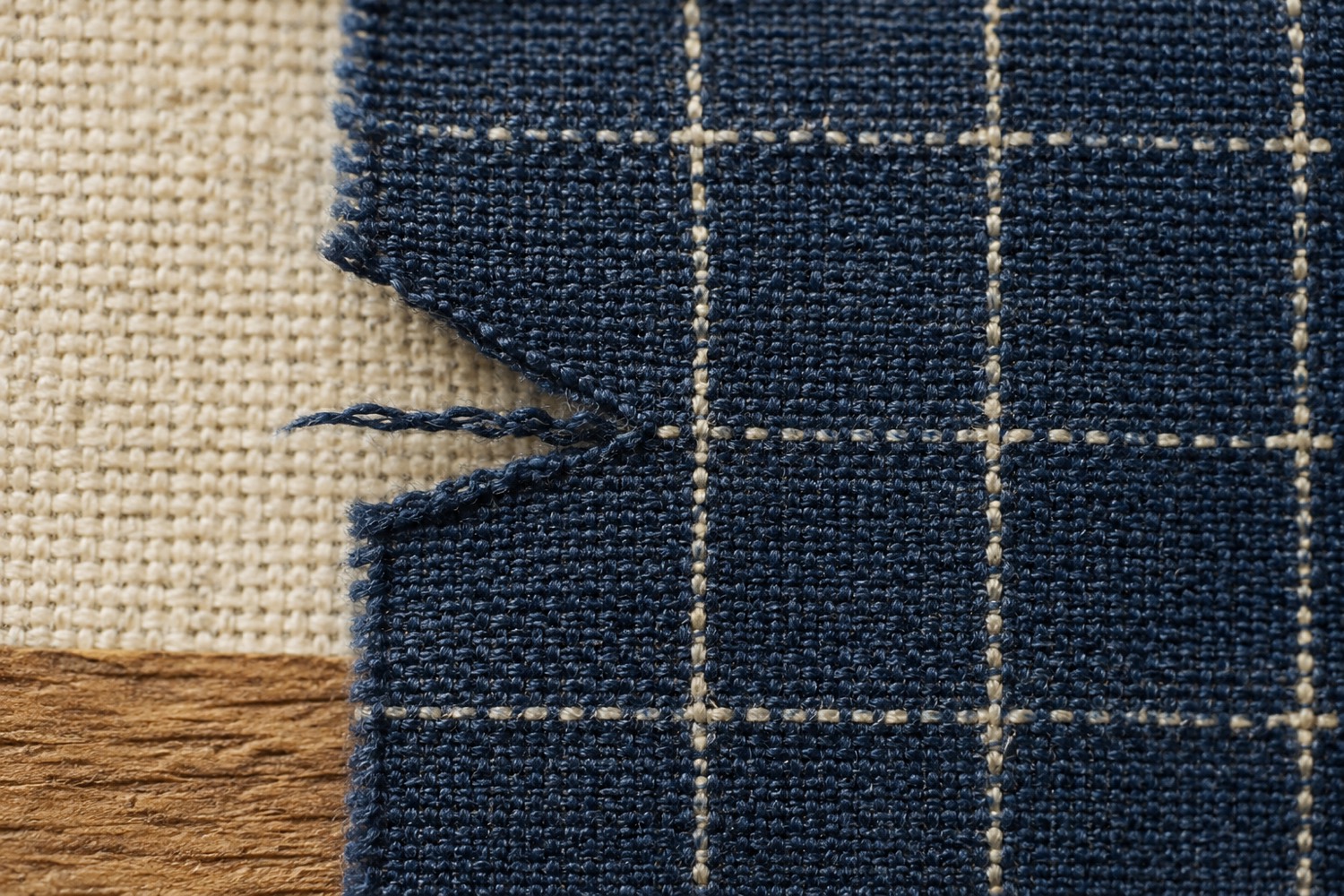 Macro view of a small tear in indigo ripstop cloth stopping cleanly where it meets a heavier grid yarn.